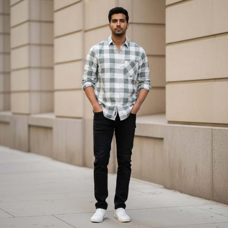 Man wearing a checkered shirt and black pants standing against a beige wall.