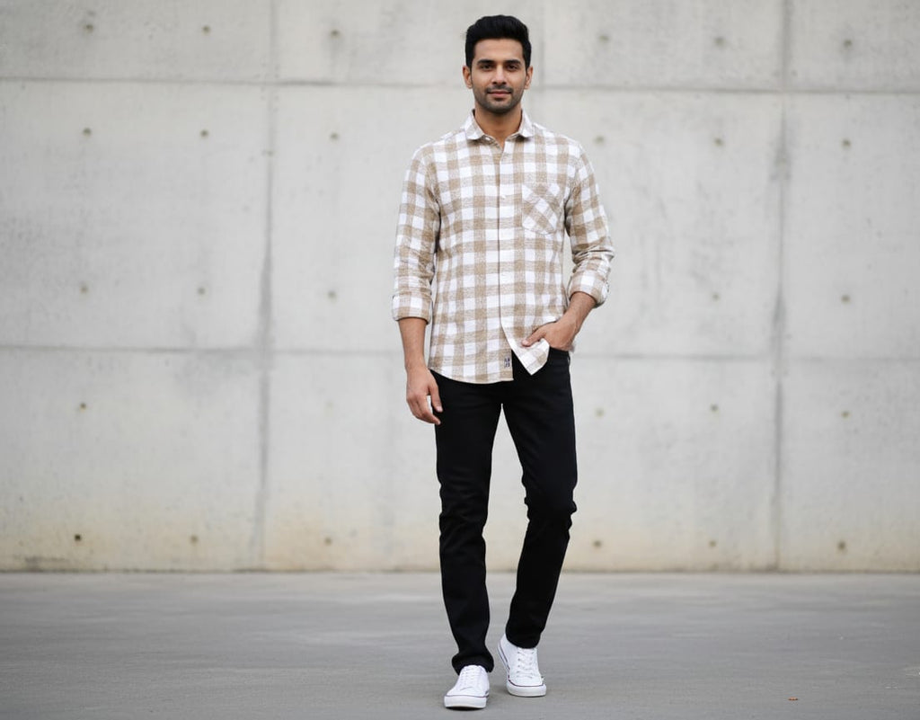 Man wearing a checkered shirt and black pants standing against a concrete wall.